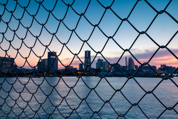 Cityscape by the sea through the grid of fence during sunset. Selective focus.