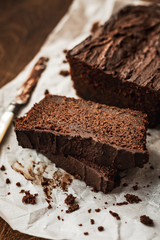 A close-up of a sliced chocolate loaf cake and a knife on baking paper on dark wooden background