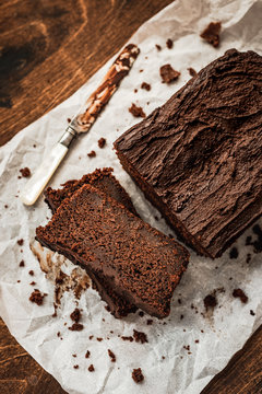 Sliced chocolate loaf cake and a knife on baking paper on dark wooden background