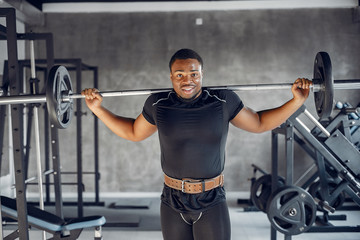 Fototapeta na wymiar Sports man in the gym. A black man performs exercises. Guy in a black t-shirt