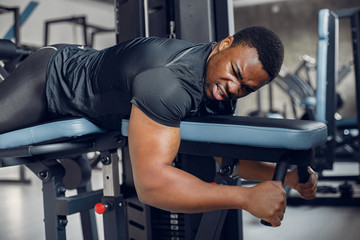 Sports man in the gym. A black man performs exercises. Guy in a black t-shirt