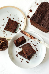 Sliced chocolate loaf cake served on two plates, a knife covered with chocolate, high key, white background