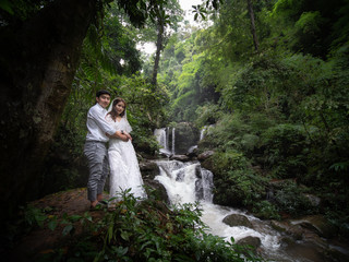 asian couple taking pre wedding photo in jungle. waterfall in Thailand. Dark greeen forest.