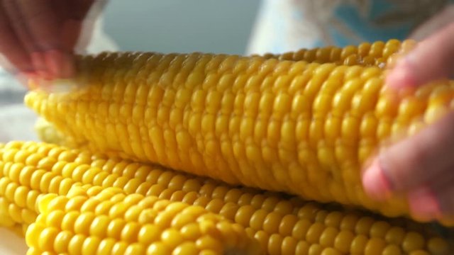 Concept on the topic of cooking corn. Close-up of the hand of a woman chef treats the corn with butter, before eating. appetizing fresh cooked corn. Selective focus, shallow depth of field