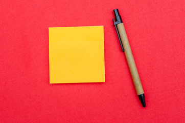 Yellow sheet of writing paper, ballpoint pen on red background, copy space, top view