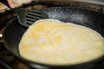 woman's hand turns a pancake with a black spatula on a frying pan close-up. concept of Breakfast