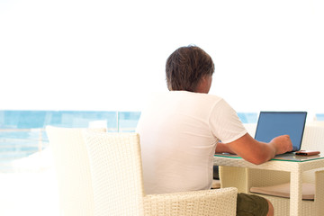 Workplace in a cafe with a sea view. Man working on a laptop in a cafe. Copy space. Mock up.