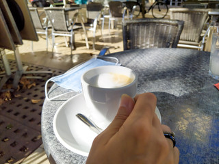 main de femme tenant une tasse de café sur une table à la terrasse d'un café
