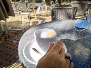 main de femme tenant une tasse de café sur une table à la terrasse d'un café