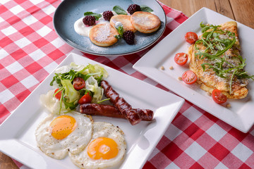 Plate of breakfast with fried eggs and sausages, and other traditional Italian dishes served on rustic wooden table.