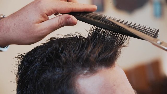 Hairdresser cutting hair of a man with scissors in a barber shop. Shot in slowmotion at 50%