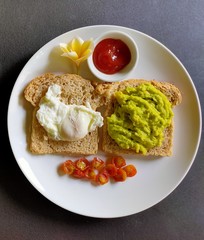 Breakfast in the morning.
brown bread in avocado jam with  poached egg
small tomato
