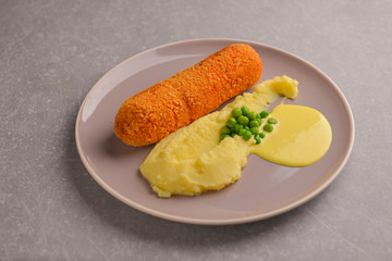 Cordon bleu cutlet, deep fried meat served with mashed potatoes and green peas on gray plate over gray background.