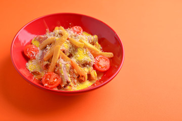 Melting cheddar cheese over the top of french fries covered in spicy sauce with meat and tomatoes. Orange background.