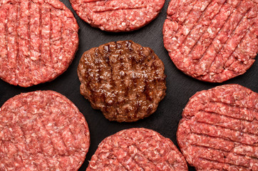 Hamburger patties top view on black table. Grilled and raw beef patties