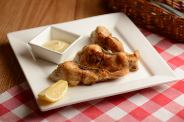 Fried fish with lemon and sauce served on white plate over wooden table with plaid tablecloth in restaurant.
