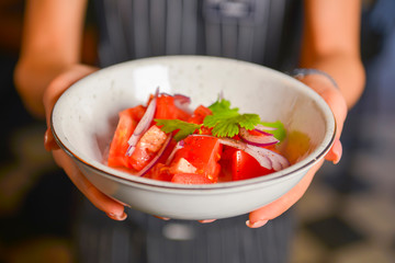 Close up of waiter serving fresh green salad with tomato and onion. Waiter in uniform at work. Restaurant service.