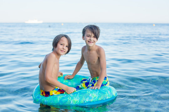 Children, preteen boys, playing on the beach with inflatable ring, having fun