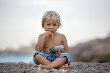 Fototapeta na wymiar Cute boy, child, eating spaghetti on the beach, enjoying dinner
