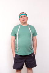 A funny fat man in a green bandana and a t-shirt with a measuring tape around his neck. half-length portrait. home fitness training, independent training.