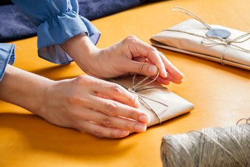 Obraz premium women wrapping gift. A parcel wrapped in paper and tied with rough twine on yellow table