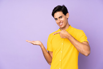 Man over isolated purple background holding copyspace imaginary on the palm to insert an ad