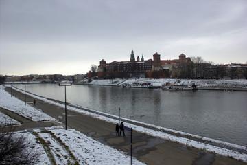Krakow, Poland - January 29, 2015: Wide angle view of famous wawel castle covered with snow next to vistual river against cloudy sky