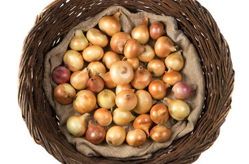 A basket of vines filled with yellow and pink onions lying on a linen bag, top view. An isolated object. Vegetable background. Concept of food, farm products.