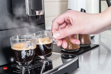 in two cups of glass of coffee Prepared on the coffee machine. A woman's hand picks up an espresso Cup