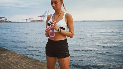 Young disabled woman drinking water from sport bottle on pier after training - Powered by Adobe
