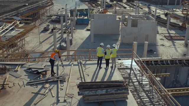 Aerial Flight Over a New Constructions Development Site with Diverse team of Engineers and Architects Discussing Real Estate Projects. Heavy Machinery and Construction Workers are Working in the Area.