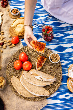 Hand holding portion of bread with sobrasada. Traditional Majorcan food. Typical cuisine of the Balearic Islands. Picnic with fruit, almonds, pastries and sausages.
