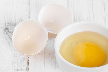 Row fresh egg in ceramic small white plate and two parts of shell on painted wooden background horizontal macro