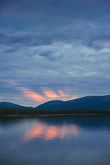 Beautiful mystical sundown in hills with clouds and reflection in the water