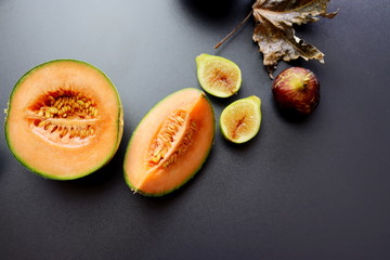 Ripe and juicy cantaloupe melon in a cut and figs on a gray background. Autumn still life with melon and figs. Autumn fruits.
