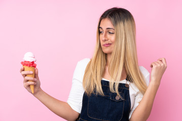 Young Uruguayan woman with a cornet ice cream over isolated pink background with sad expression