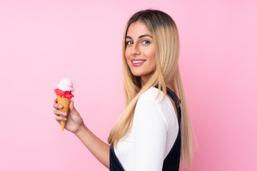 Young Uruguayan woman with a cornet ice cream over isolated pink background smiling a lot