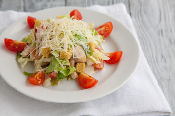 Tasty Caesar salad in a white plate on a wooden background. Close up.