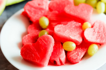 Fresh juicy watermelon slice with cut out heart shape, with fresh grapes, on plate, on concrete background