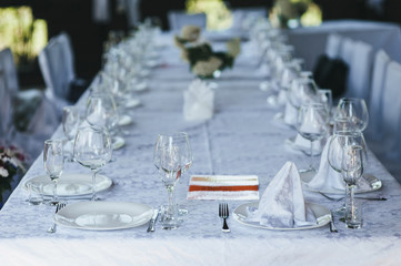 Empty glass goblets, wine glasses, plates, forks stand in a row on a table with a white tablecloth in a restaurant for guests and parties. Dishes for food, banquet.