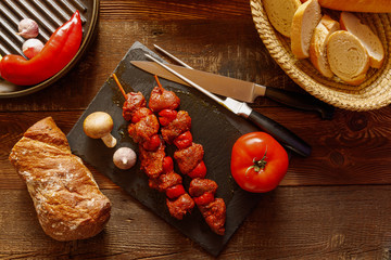 bbq skewer of beef and tomato on slate plate with garlic and mushroom bread in basket chilli pepper and cast-iron grill pan