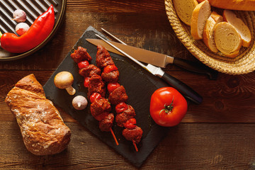 bbq skewer with beef tomato on slate plate with garlic mushroom meat knife and fork bread in basked red chilli pepper in cast-iron grill pan