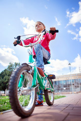 A girl in ripped jeans rides a bicycle in the park. Bottom view
