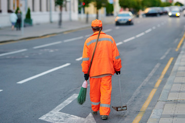 Man cleaner sweeping street with broom, municipal worker in uniform with broomstick and scoop for garbage in hands, cleaning service. Male janitor with broom and dustpan, cleaning city from garbage.