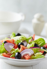 Healthy salad with black olives, tomatoes and red onion on bright wooden background.	
