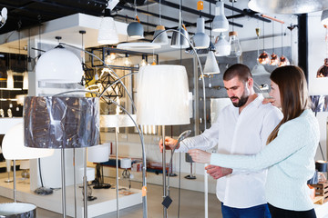 Portrait of young family couple looking floor lamp in furniture shop..