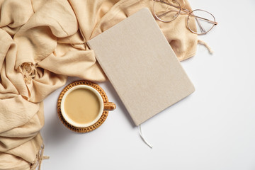 Hygge style feminine workspace with beige plaid, coffee cup, paper notebook, glasses on white background. Flat lay, top view.