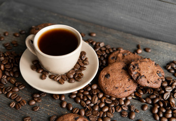 Coffee cup with cookies on wooden table background. Mug of black coffee with scattered coffee beans and cookies on a wooden table. Fresh coffee beans.