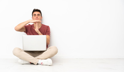 Teenager man sitting on the flor with his laptop making time out gesture