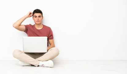 Teenager man sitting on the flor with his laptop with an expression of frustration and not...